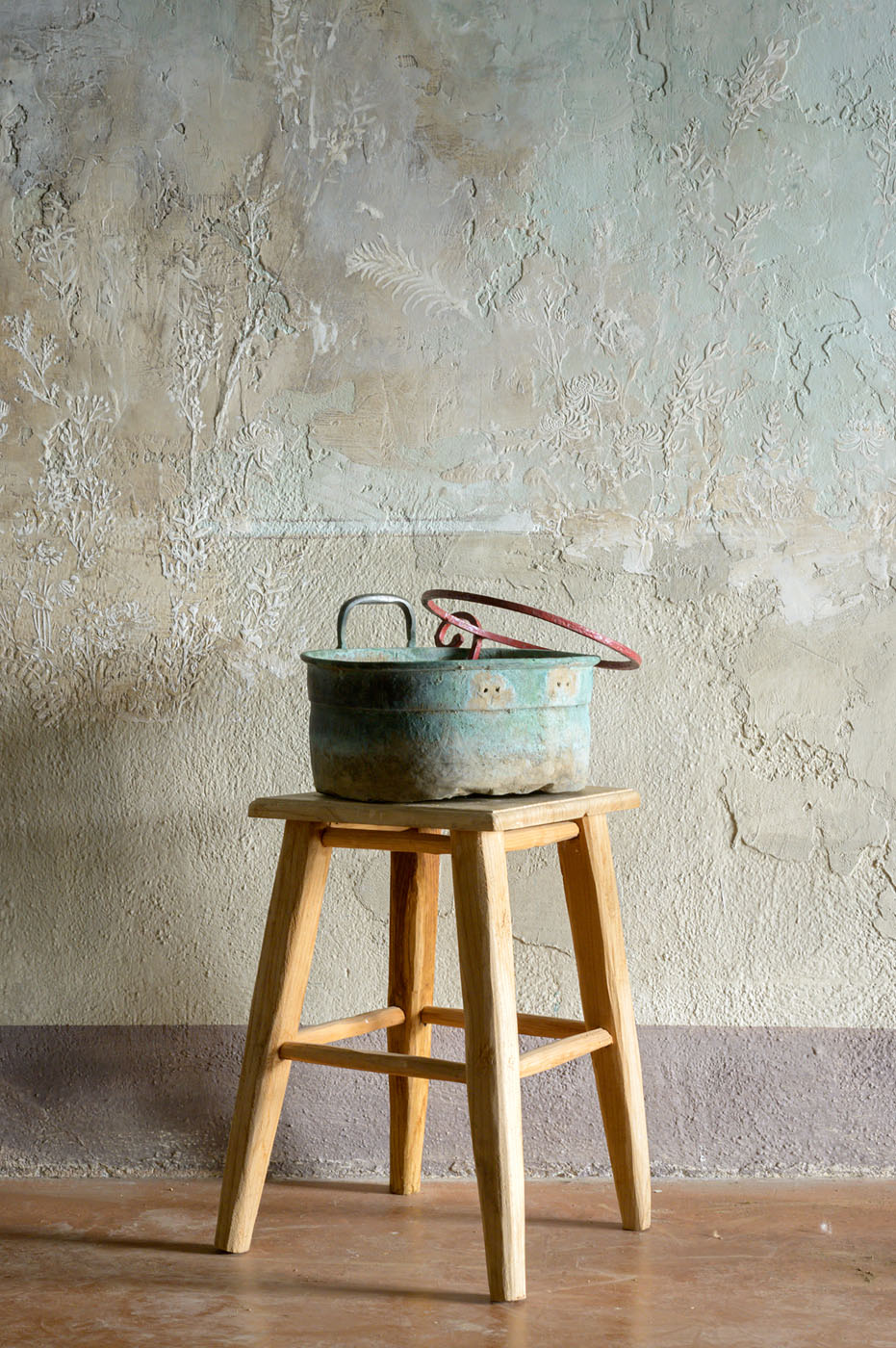 Pittura murale a bassorilievo con terre, argille, blu e ocre; in primo piano una pentola vintage.